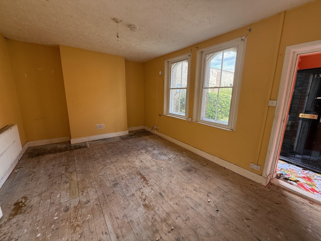 Lot: 110 - THREE-BEDROOM END-TERRACE COTTAGE FOR IMPROVEMENT - Living room with two windows to the front and entrance porch